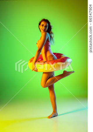 Beautiful girl in fashionable swimsuit isolated on gradient studio background in neon light. Summer, resort, fashion and weekend concept Beautiful girl in fashionable swimsuit isolated on gradient studio background in neon light. Summer, resort, fashion and weekend concept 66547904