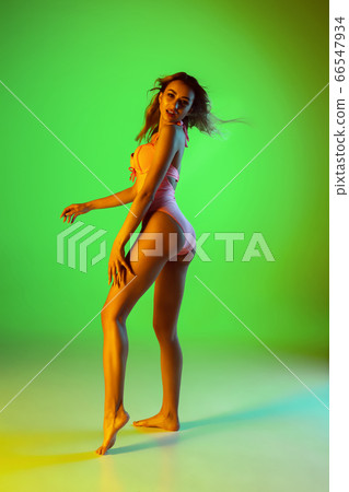 Beautiful girl in fashionable swimsuit isolated on gradient studio background in neon light. Summer, resort, fashion and weekend concept Beautiful girl in fashionable swimsuit isolated on gradient studio background in neon light. Summer, resort, fashion and weekend concept 66547934