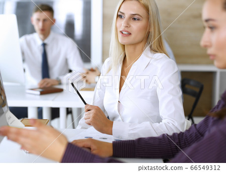 Group of business people discussing questions at meeting. Headshot of blonde businesswoman while smiling to her colleague at office negotiation. Teamwork and cooperation in corporate occupation 66549312