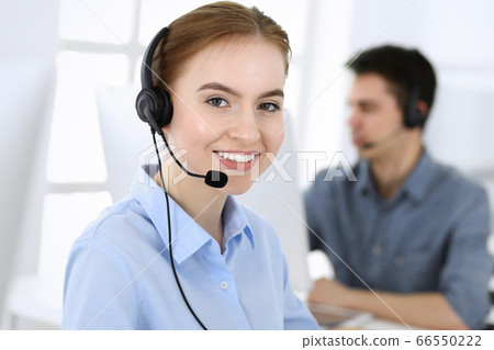 Group of operators at work. Call center. Focus on beautiful woman receptionist in headset at customer service. Business concept and casual clothing style Group of operators at work. Call center. Focus on beautiful woman receptionist in headset at customer service. Business concept and casual clothing style 66550222