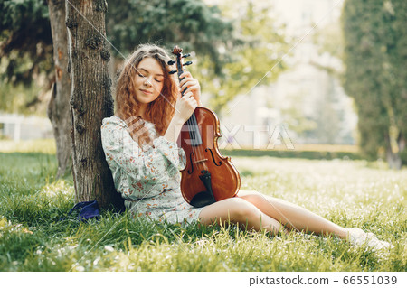 Beautiful girl in a summer park with a violin Beautiful girl in a summer park with a violin 66551039