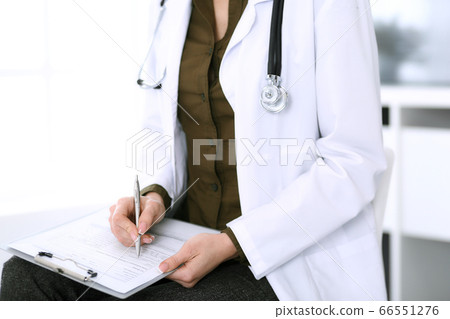 Woman doctor writing something at clipboard while sitting at the chair, close-up. Therapist at work filling up medication history records. Medicine and healthcare concept 66551276