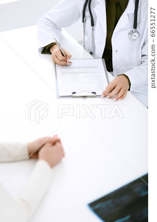 Woman doctor and patient sitting and talking at medical examination at hospital office, close-up. Therapist filling up medication history records. Medicine and healthcare concept 66551277