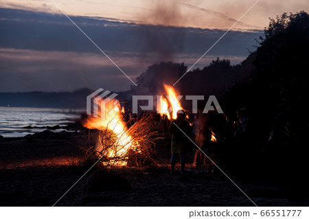 Unrecognisable people celebrating summer solstice with bonfires on beach 66551777