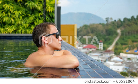 handsome man in sunglasses leans on hotel pool edge handsome man in sunglasses leans on hotel pool edge 66551804