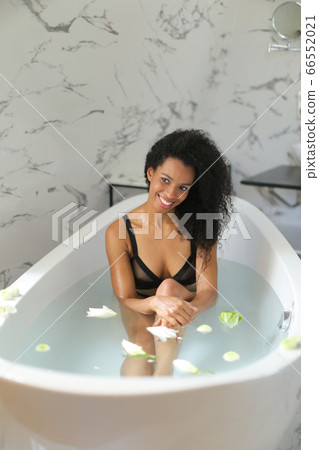Black young smiling woman taking bath with flowers and wearing swimsuit. 66552021