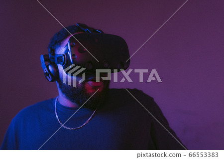 The guy is playing VR games. Neon blue light. 66553383