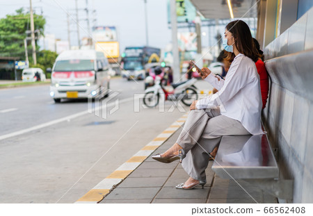 young woman holding smartphone and waiting for bus 66562408