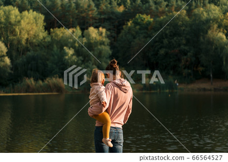 Mother and baby girl sitting near lake. Local travel. New normal vacation. Mother's day Mother and baby girl sitting near lake. Local travel. New normal vacation. Mother's day 66564527