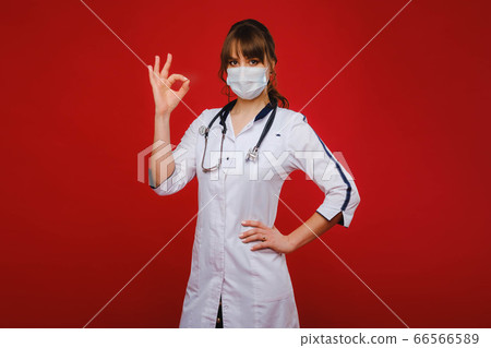 A young doctor stands on a red background and shows his hand everything will be fine. The doctor shows OK. A young doctor stands on a red background and shows his hand everything will be fine. The doctor shows OK. 66566589