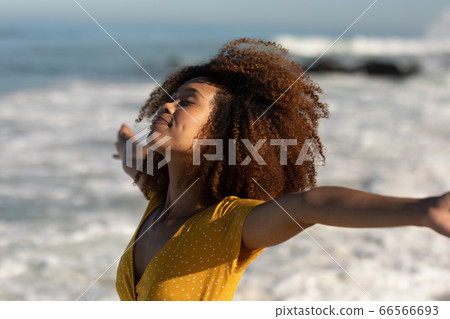 A mixed race woman with her arms outstretched on beach on a sunny day A mixed race woman with her arms outstretched on beach on a sunny day 66566693