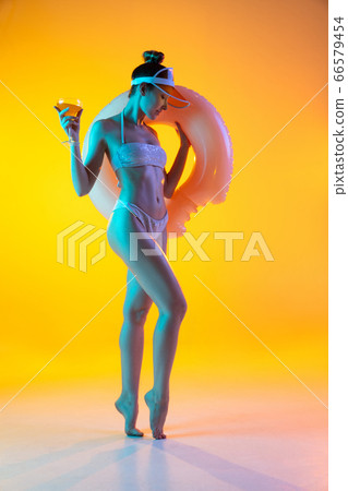 Fashion portrait of seductive girl in stylish swimwear posing on a bright yellow background. Summertime, beach season 66579454