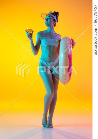 Fashion portrait of seductive girl in stylish swimwear posing on a bright yellow background. Summertime, beach season 66579457