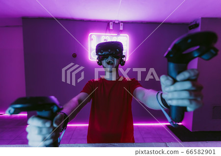 VR E-Sports. The guy is playing an online shooter in the game neon room. VR E-Sports. The guy is playing an online shooter in the game neon room. 66582901