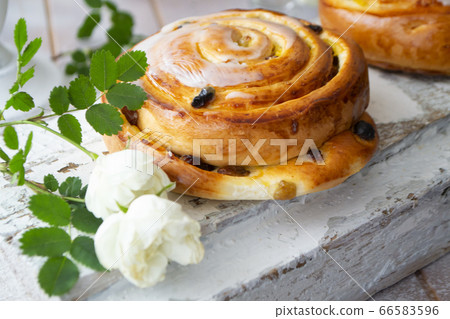 Raisin bun. Bun with raisins and vanilla cream close-up on white shabby background with vintage white roses 66583596