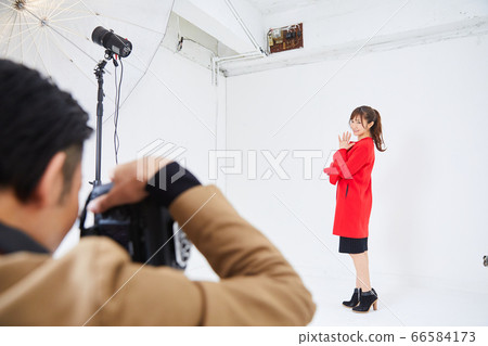 Young female model in red coat and photographer Young female model in red coat and photographer 66584173