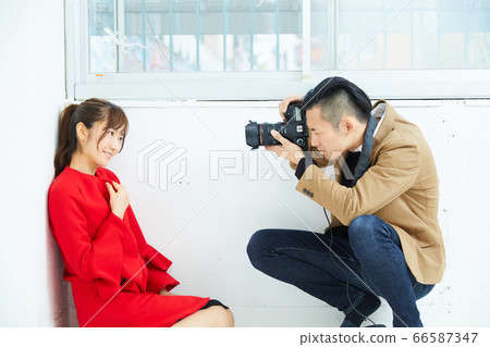 Young female model in red coat and photographer Young female model in red coat and photographer 66587347
