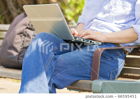 Workers A male remote worker who operates a computer in a casual style on a bench in a park 66595451