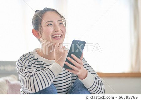 年輕女子看著床上的智能手機 66595769