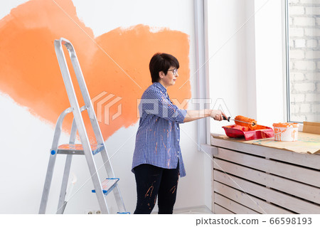 Renovation, redecoration and repair concept - middle-aged woman painting wall in new home. Renovation, redecoration and repair concept - middle-aged woman painting wall in new home. 66598193