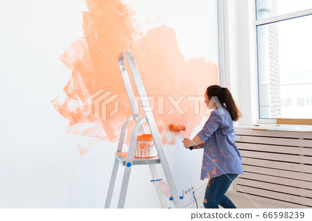 Pretty smiling woman painting interior wall of home with paint roller. Redecoration, renovation, apartment repair and refreshment concept. Pretty smiling woman painting interior wall of home with paint roller. Redecoration, renovation, apartment repair and refreshment concept. 66598239
