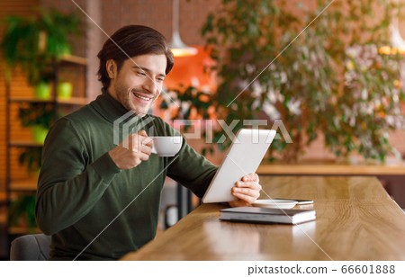 Happy young businessman reading news while drinking coffe at cafe Happy young businessman reading news while drinking coffe at cafe 66601888