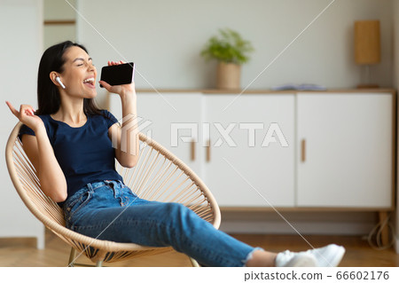Woman Listening To Music On Smartphone Singing Song At Home 66602176