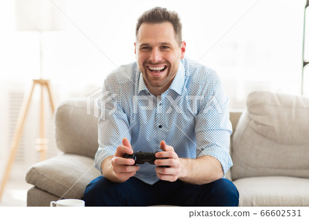 Young man sitting on couch playing video games Young man sitting on couch playing video games 66602531