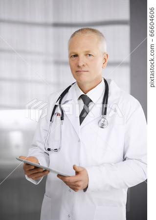 Elderly confident doctor standing straight and using tablet in clinic. Perfect medical service. Medicine and healthcare concept Elderly confident doctor standing straight and using tablet in clinic. Perfect medical service. Medicine and healthcare concept 66604606