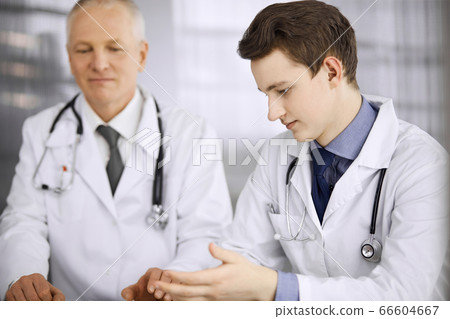 Doctors colleagues and elderly therapist discussing current disease therapy while sitting at working place in clinic. Teamwork in hospital. Medicine and healthcare concept Doctors colleagues and elderly therapist discussing current disease therapy while sitting at working place in clinic. Teamwork in hospital. Medicine and healthcare concept 66604667