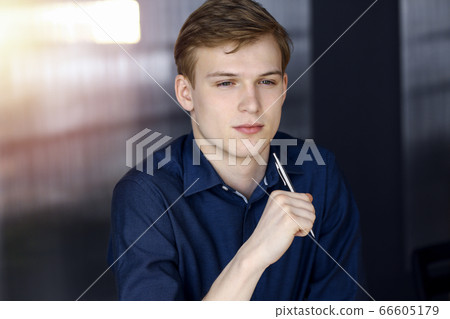 Young blond businessman thinking about strategy at his working place with computer in a darkened office, glare of light on the background Young blond businessman thinking about strategy at his working place with computer in a darkened office, glare of light on the background 66605179