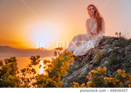 Young woman in long dress standing on a rock 66606407