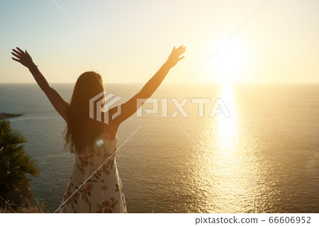 woman in summer dress raises hands on beach at sunset 66606952