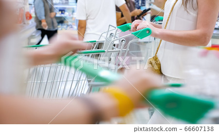 Woman without face in a white suit with a trolley in a store. Unrecognizable shoppers pass by 66607138