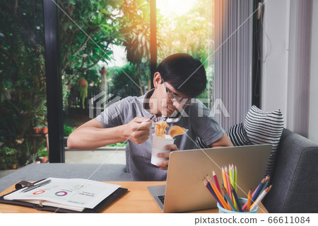 A man who works from home is busy talking on the phone and eating instant noodles. A man who works from home is busy talking on the phone and eating instant noodles. 66611084