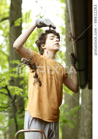closeup photo of teenager boy cleaning roof from old leafs 66612263