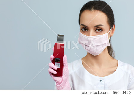 beautician in mask is holding Ultrasonic scraber. 66613490