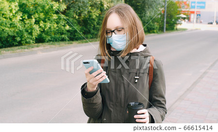 Student girl in a protective medical mask and glasses writes a text message, reads news, surfs the Student girl in a protective medical mask and glasses writes a text message, reads news, surfs the 66615414