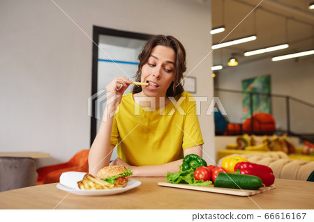 Woman with french fries looking at fresh vegetables Woman with french fries looking at fresh vegetables 66616167