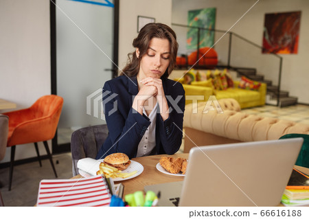 Thinking young woman sitting and looking at food in plates Thinking young woman sitting and looking at food in plates 66616188