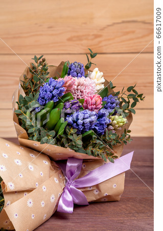 bouquet of flowers with multi-colored hyacinths in a craft paper package on a wooden background. high quality. 66617009