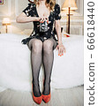 Sexy girl in stockings and retro dress with vintage camera in hand sitting on a white bed in high heels 66618440