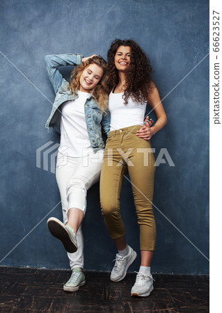 young pretty teenage girls friends with blond and brunette curly hair posing cheerful on blue background, lifestyle people concept young pretty teenage girls friends with blond and brunette curly hair posing cheerful on blue background, lifestyle people concept 66623527