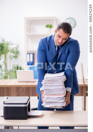 Young male employee making copies at copying machine 66624284