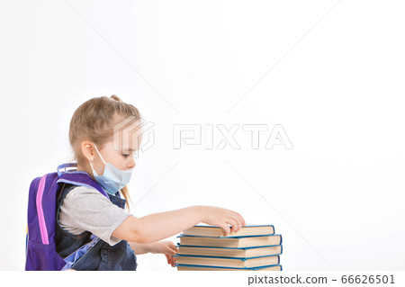 a first-grader learns to read. a little girl on home distance learning. A child in a medical mask reads a book. the student is doing homework. isolated on a white background 66626501