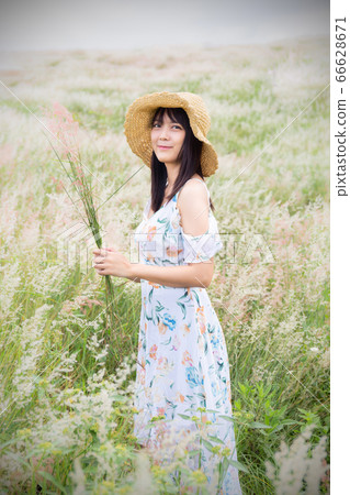 The girl wearing a hat, wearing a white dress, standing in the middle of the grass with beautiful white flowers with a relaxed and happy mood. Gray frame 66628671