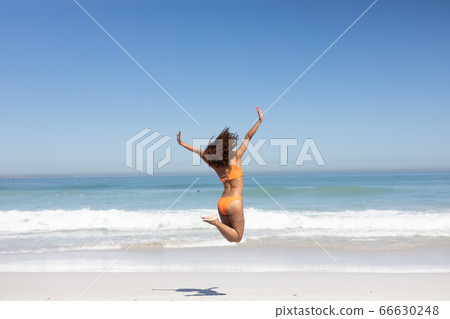 Mixed race woman jumping on the beach Mixed race woman jumping on the beach 66630248
