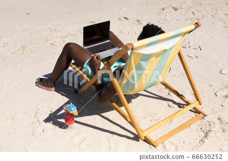 African American man using computer on the beach African American man using computer on the beach 66630252