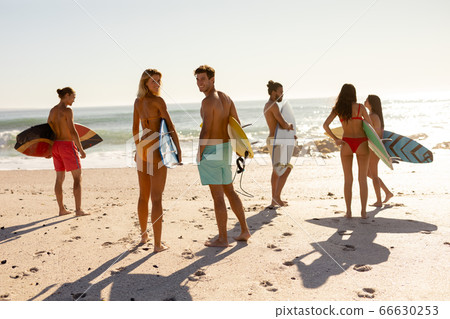 Young mixed race people holding surf boards on beach Young mixed race people holding surf boards on beach 66630253