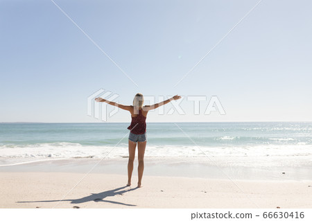 Young caucasian woman raising arms on the beach 66630416